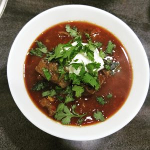 Bowl of Texas chili garnished with sour cream and fresh cilantro
