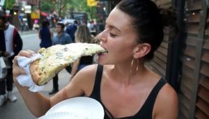 Christine taking a bite of a gian slice of white sauce pizza