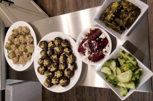 Happy hour appetizers including pork meatballs, stuffed mushrooms, beets with feta, cucumbers, and dolmades